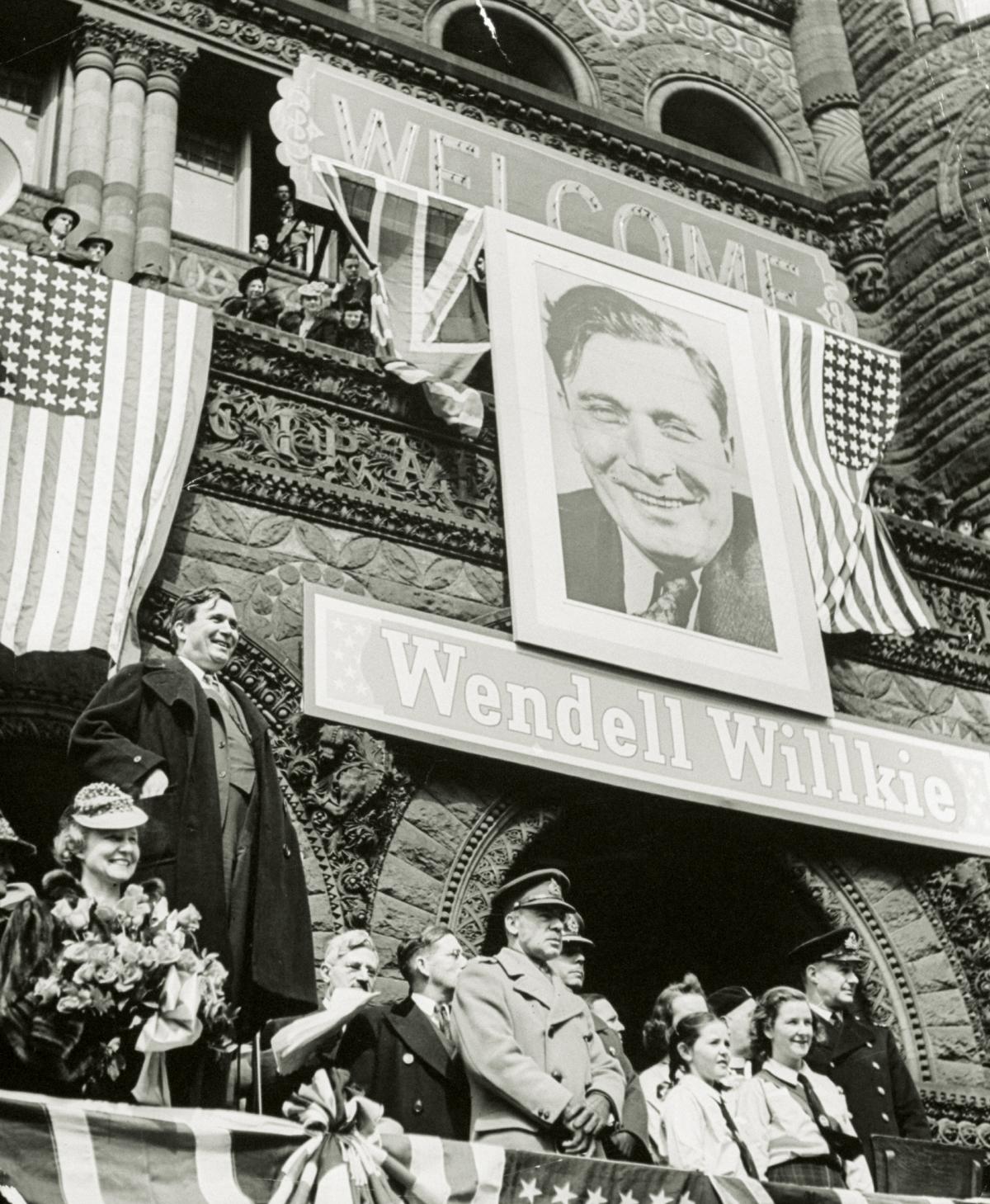 black and white photograph of a campaign photo and sign, people on a stage