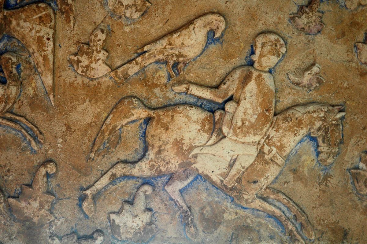 stucco falconer riding a horse, with a large falcon perched on his right arm, extended behind him