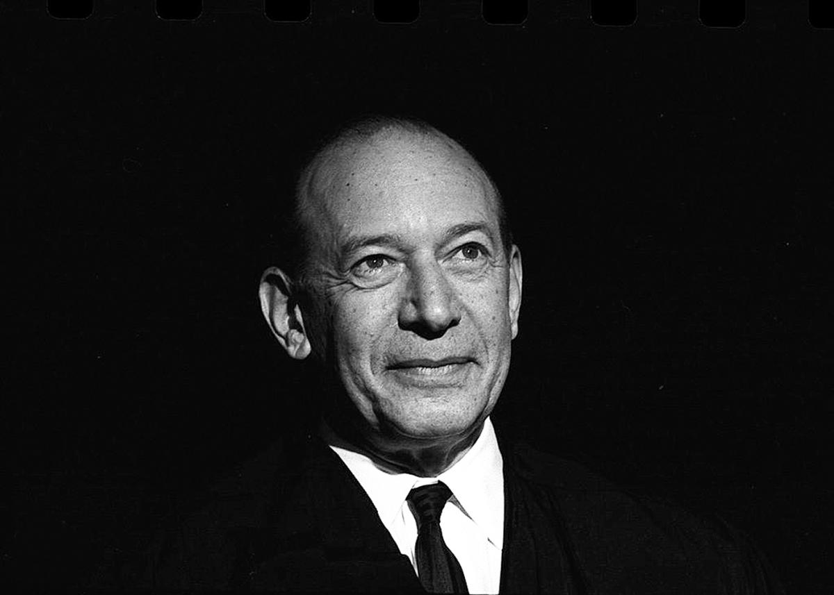 Black and white photo of Fortas, looking off into the distance, smiling slightly, wearing a dark suit and tie