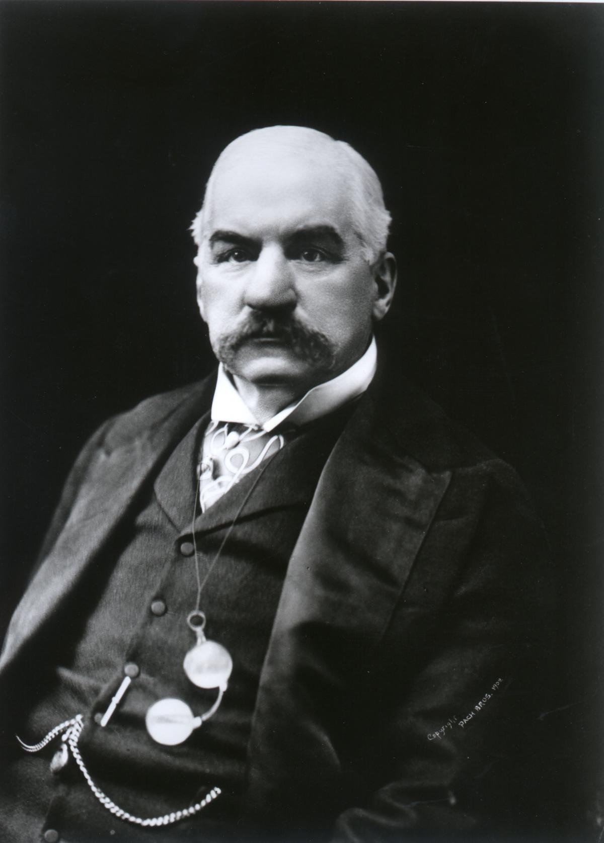 Morgan wearing a black coat, vest, and a watch chain, with a thick moustache