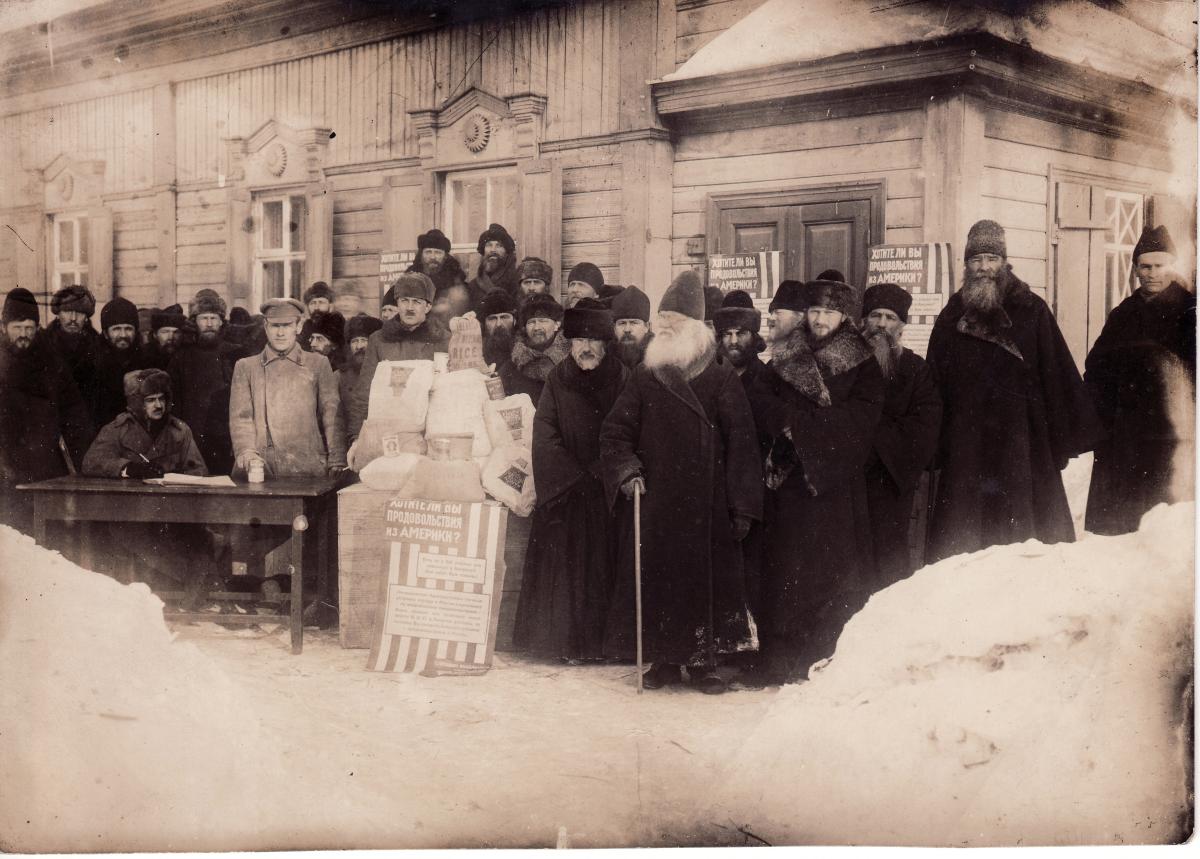 Russian priests, dressed in heavy coats and furs, stand in the snow awaiting rations from government officials