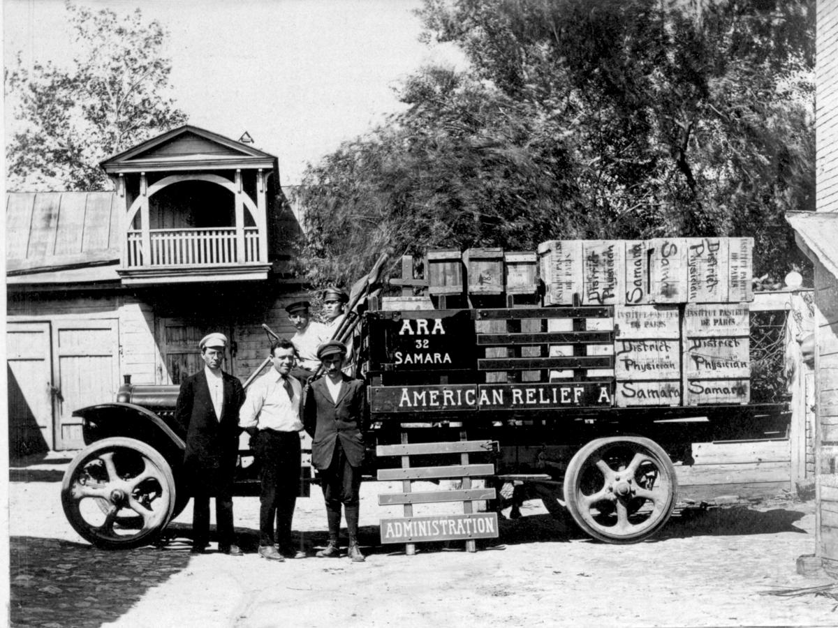 Three men stand in front of a truck loaded with crates of food