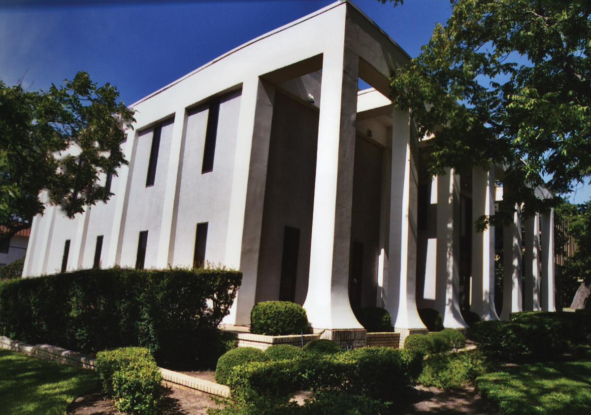 Blocky white stucco building, fringed with trees and bushes