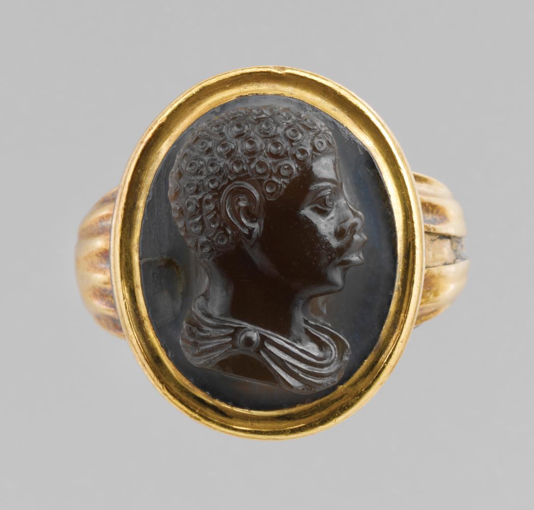 Gold frame with a black stone in the center, carved with the profile of a young African boy