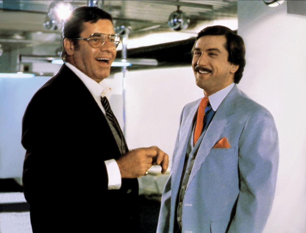 De Niro, in glasses and a dark suit, shares a laugh with Lewis, wearing a powder blue suit and orange tie