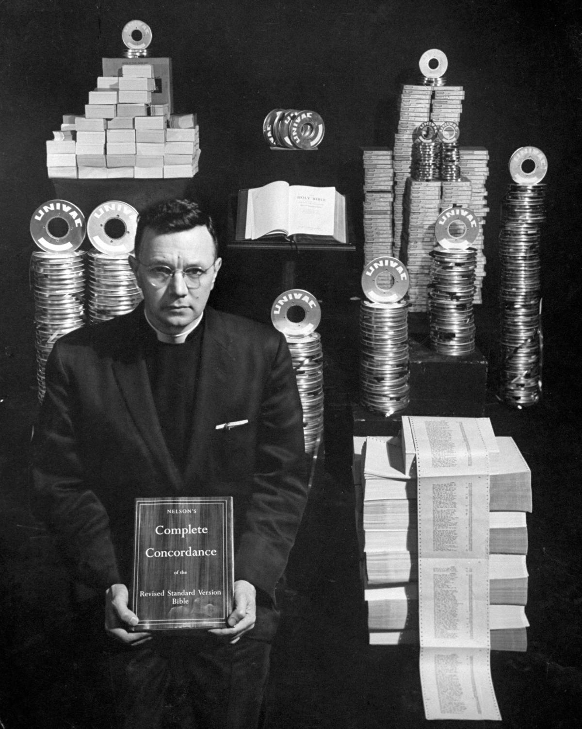 Black and white photo of a man standing in front of tape canisters and computer print outs