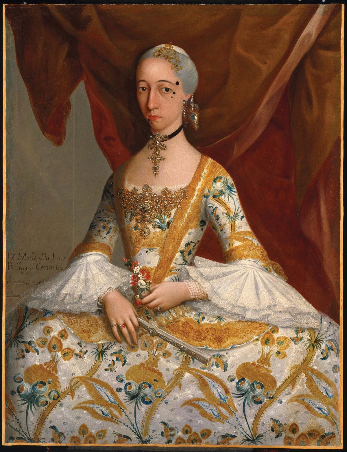 Wearing an embroidered white and gold dress with wide lace sleeves, with several large birthmarks on her face and chin