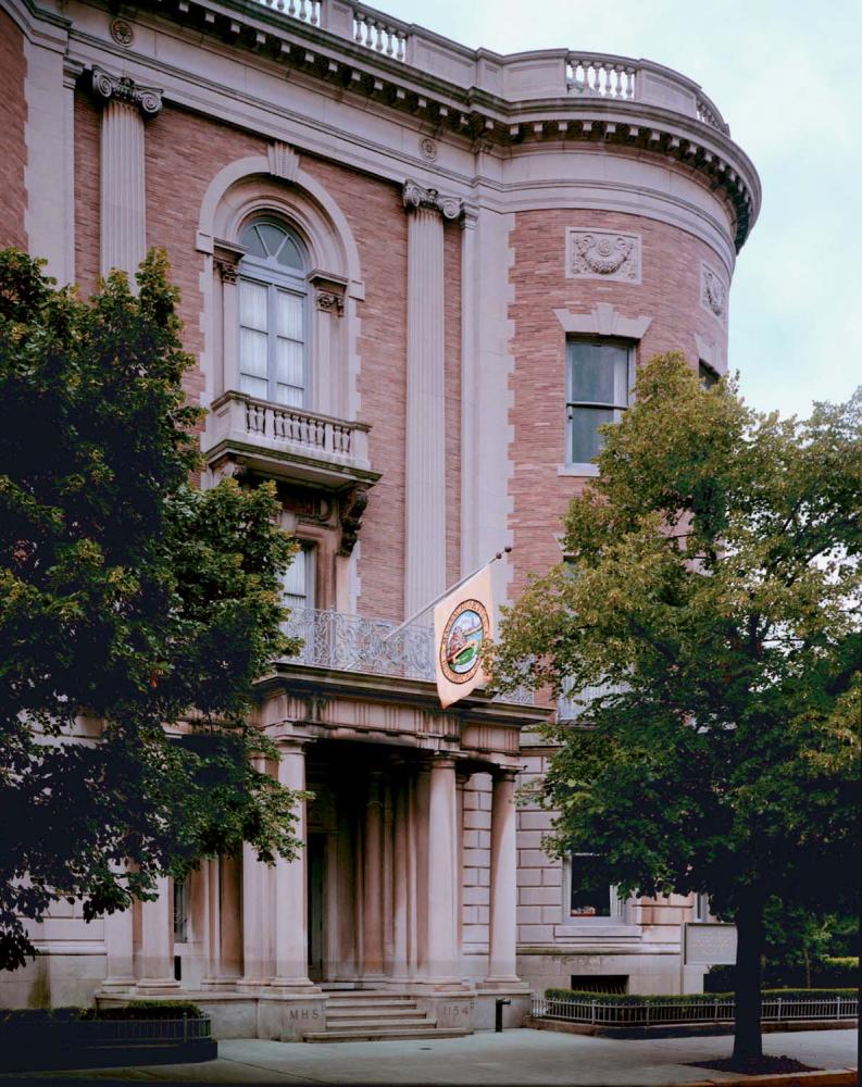 Brown brick facade, with white columns, of the Historical Society building, flanked by trees