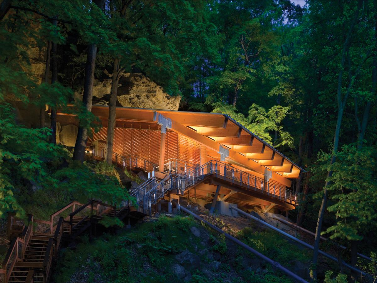 Meadowcroft Rockshelter, surrounded by thick green forest, lit up at dusk