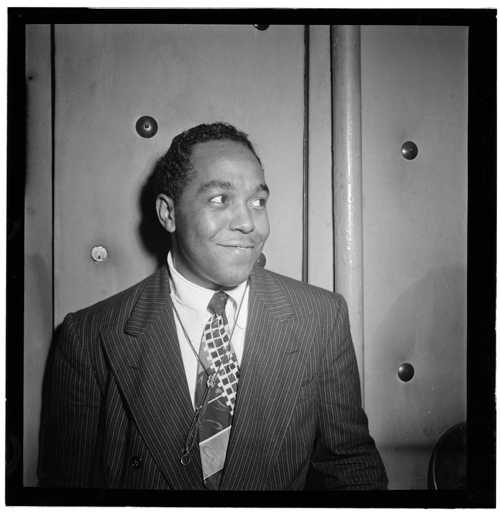 Parker, looking off to his left and smiling, wearing a dark suit and patterned tie