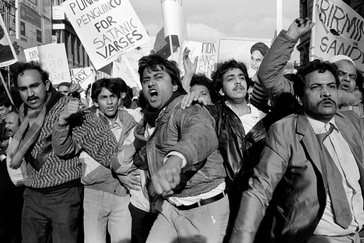 black and white photo of a crowd protesting the fatwah, holding signs, yelling and pushing forward