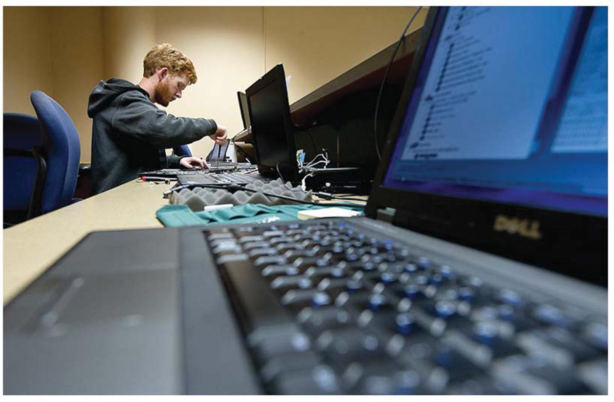 Close up view of a laptop keyboard, with a Berea student working in the background