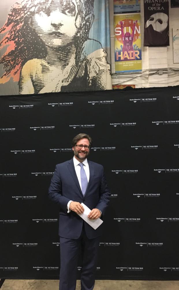 photograph of a man in front of a black wall advertising the vietnam war documentary