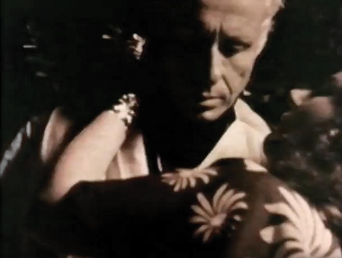 film still of a man embracing a woman, looking over her shoulder