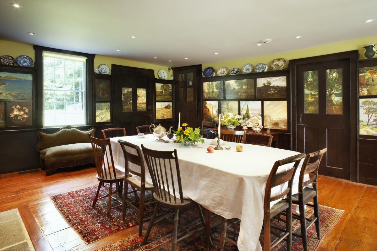 Photograph of a dining room with a table, painted panels in the background