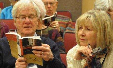 two audience members, one man holds a book