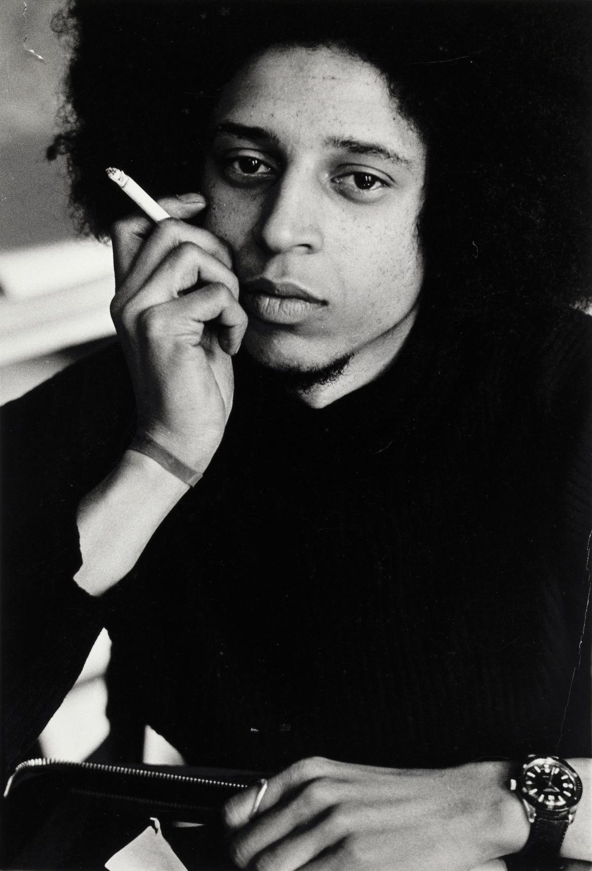 An intimate portrait of a young Black man seated and holding a cigarette