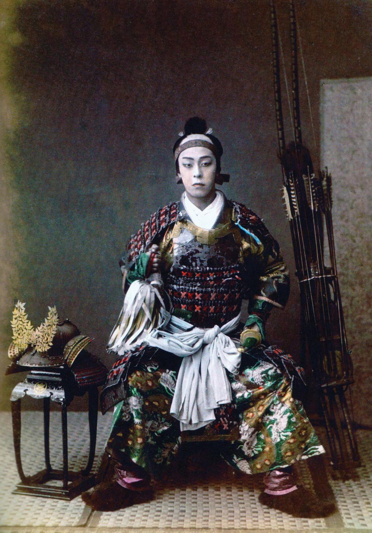 A color-tinted photograph of a samurai sitting in 1867.