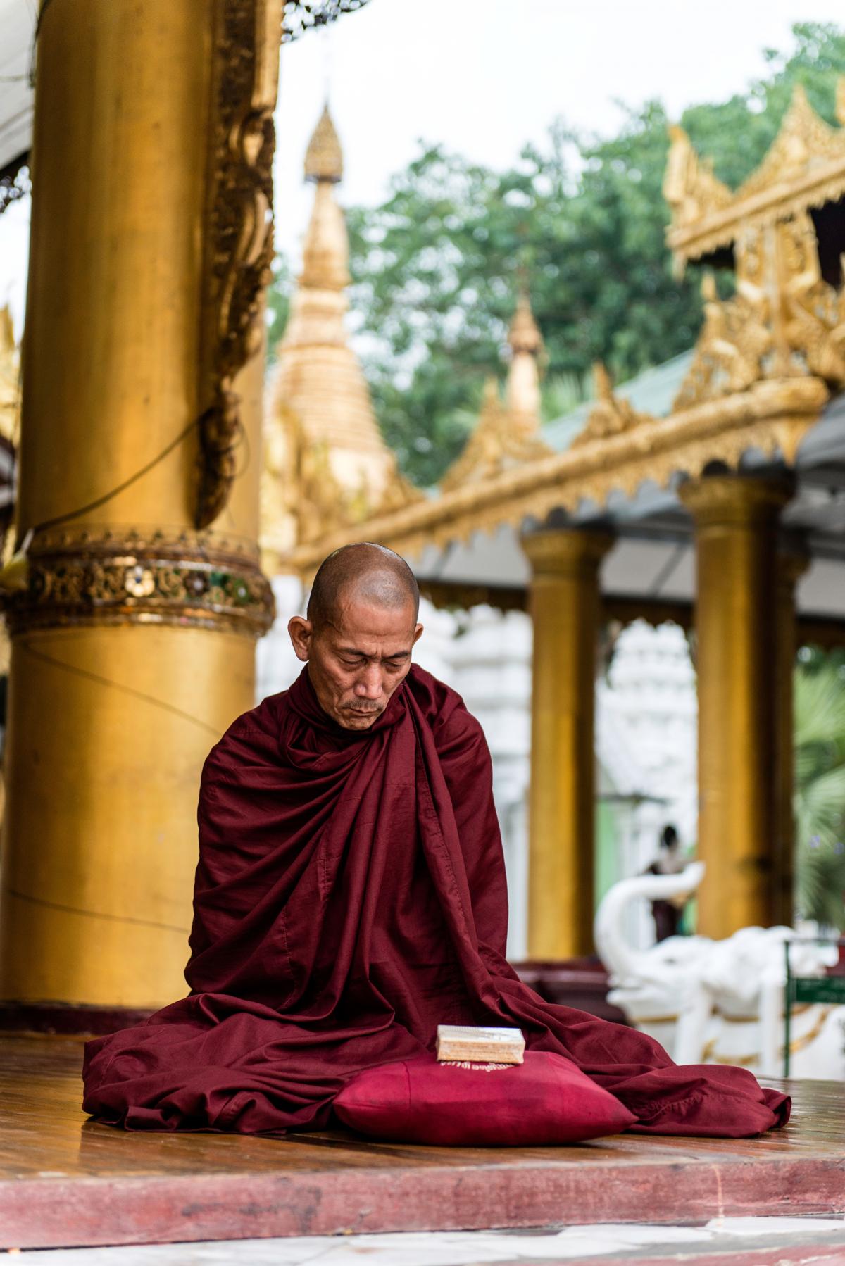 a modern Buddhist monk in a red robe sits and meditates in a temple