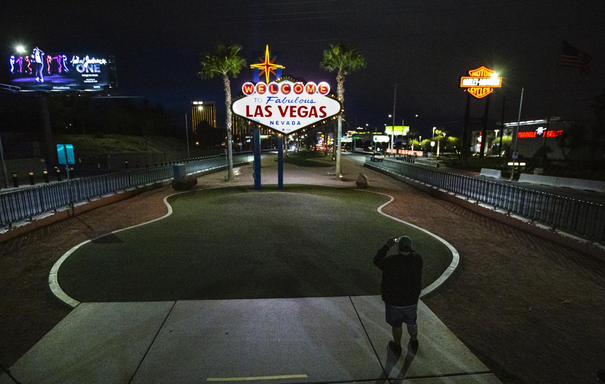 photograph of man taking photo of Las Vegas sign on deserted street