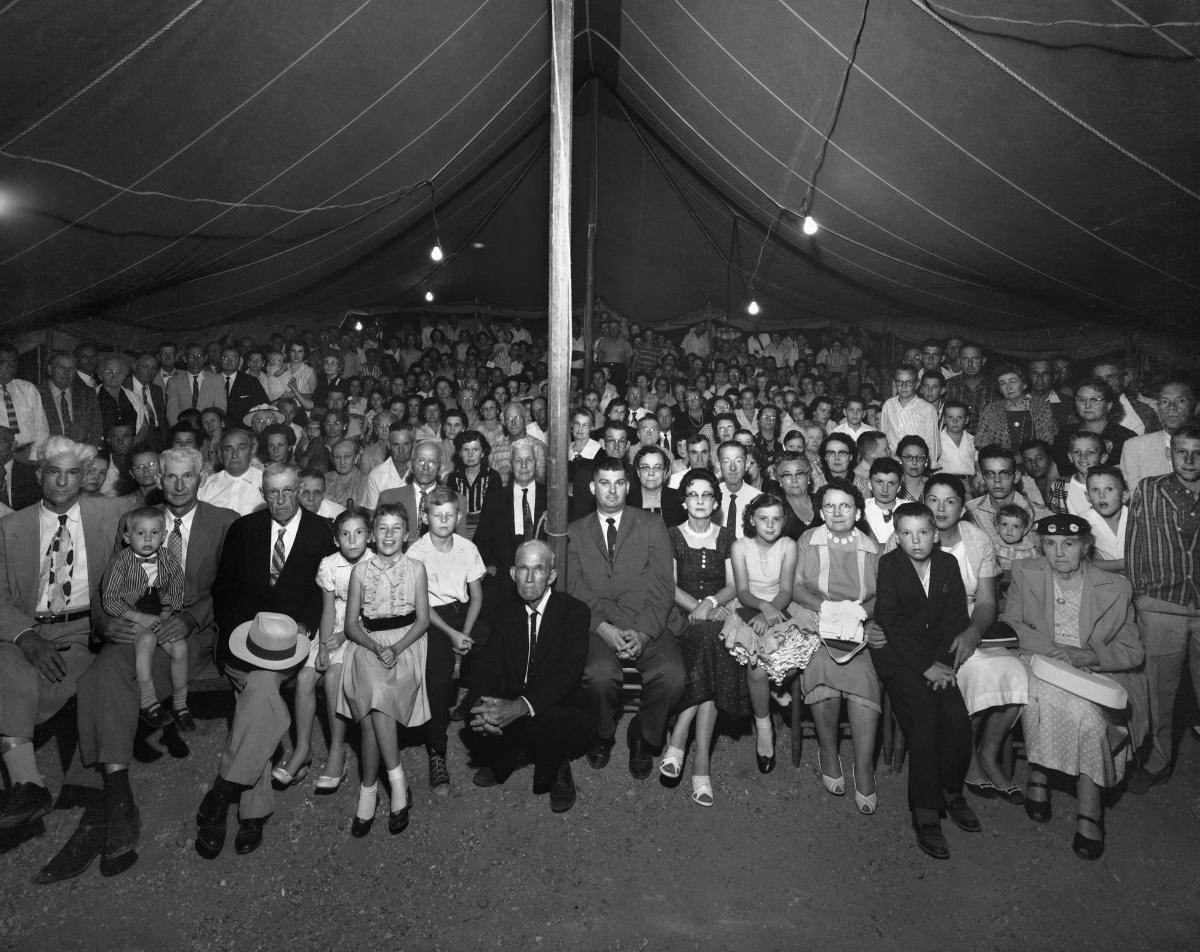 a white crowd gathered under a tent