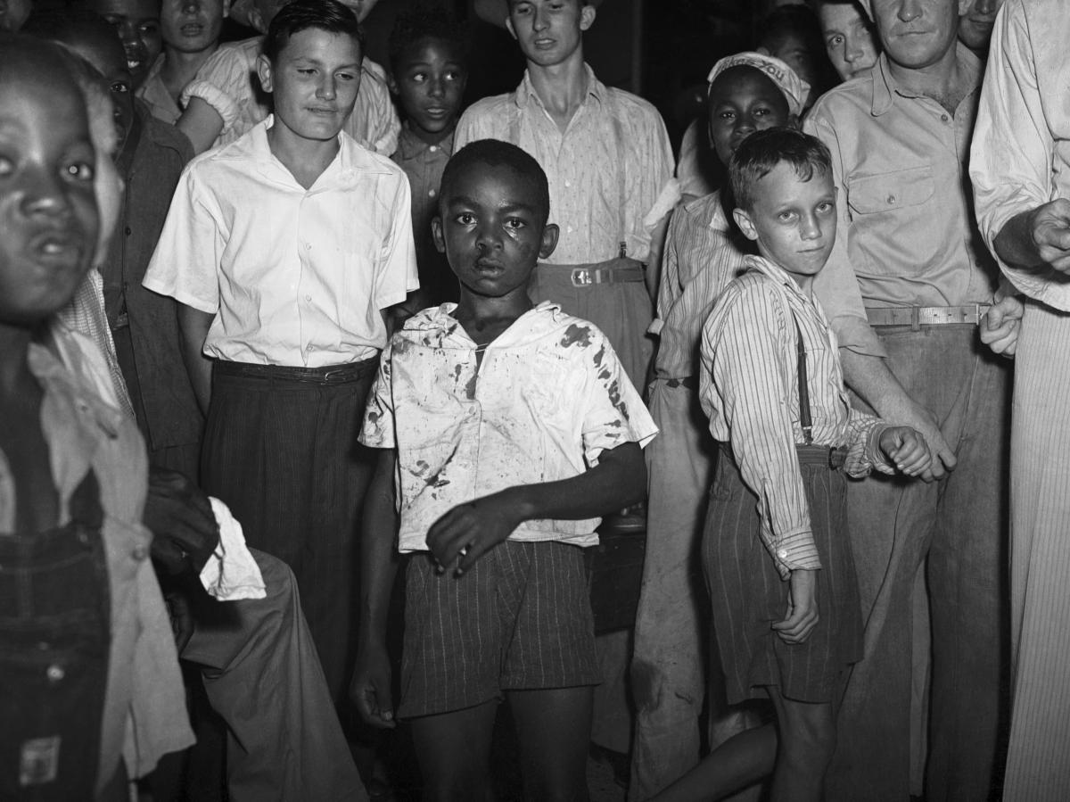  a black and white crowd centers on a young Black boy with blood stains on his clothes