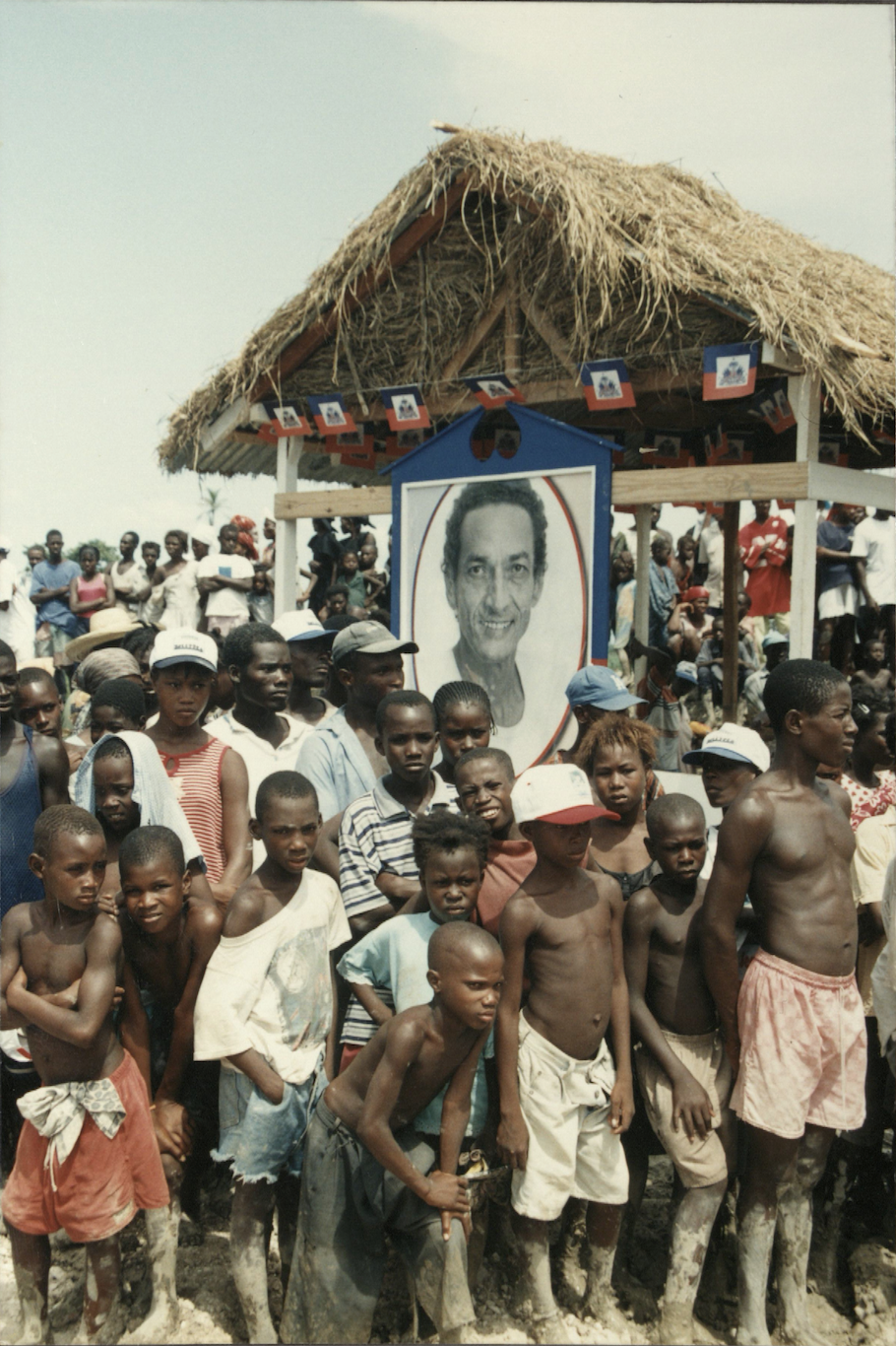 Children in L’Estère, in Haiti’s Artibonite Valley, stand with a poster of Jean Dominique on July 31, 2000, nearly four months after his assassination. 