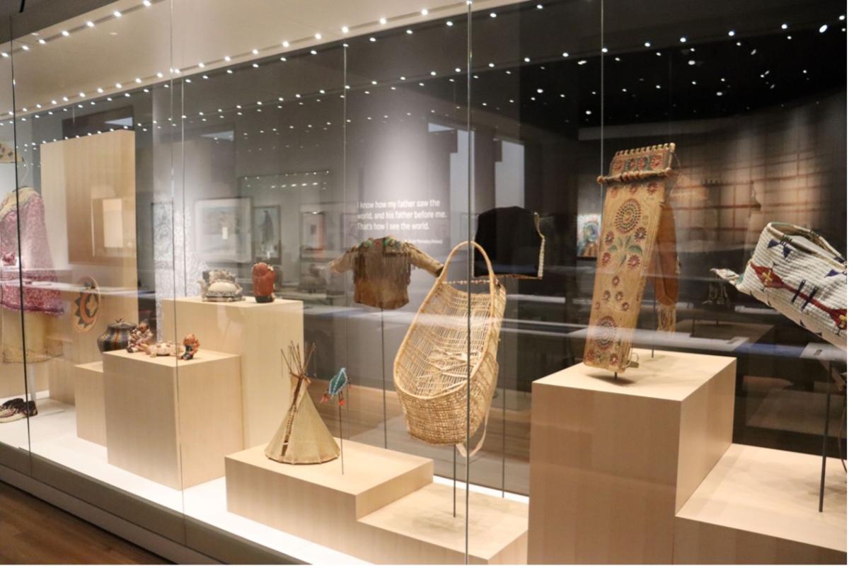 A display of baskets, clothing, and other Native American art in glass cases.