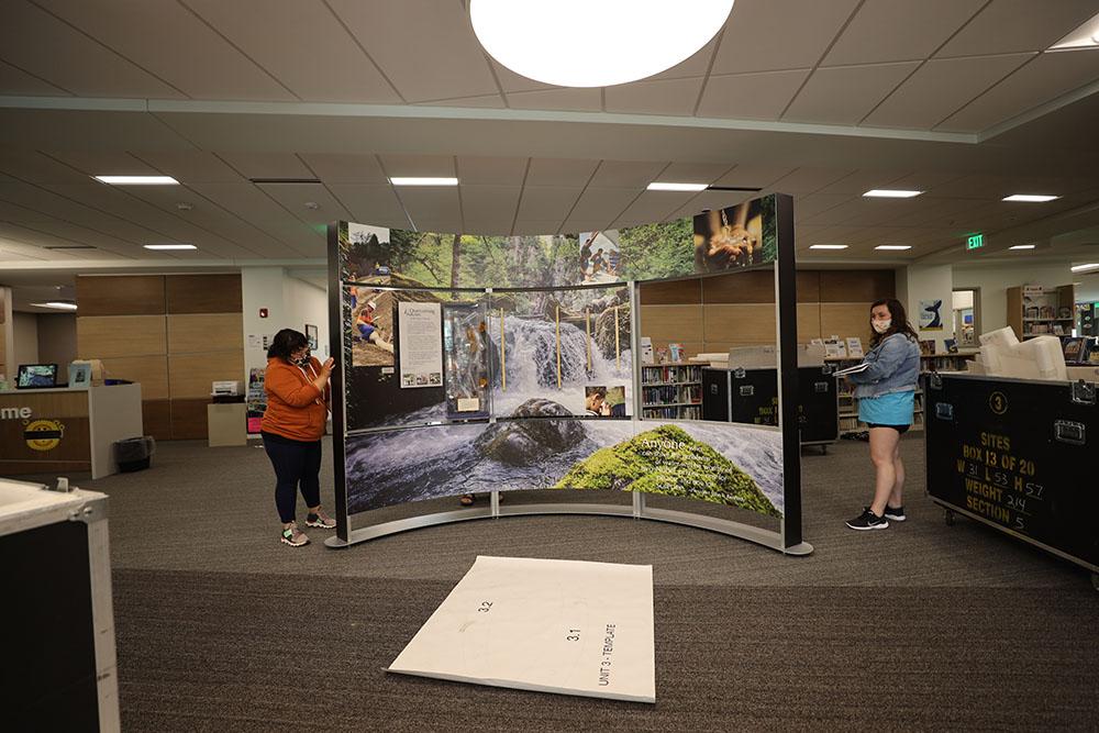 Director of Programs Megan Telligman (left) installs the Smithsonian’s Water/Ways exhibit at the North Webster Community Public Library.