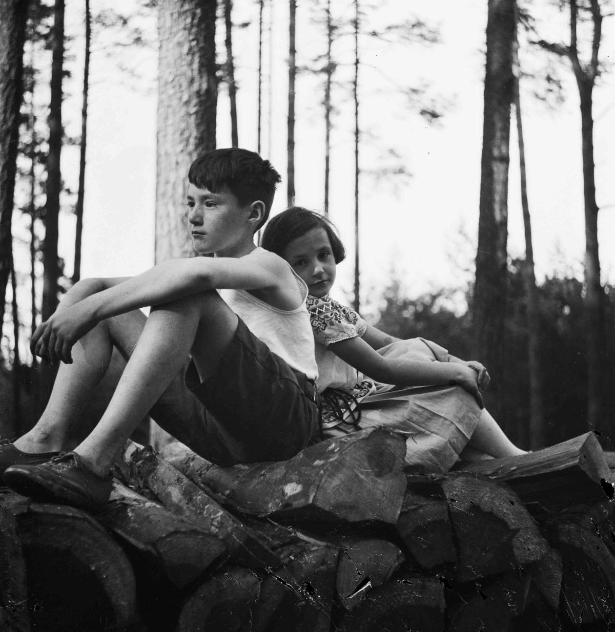 black and white photo of brother and sister leaning against each other in the woods