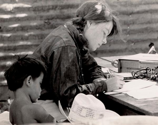Woman writing on paper with a child next to her