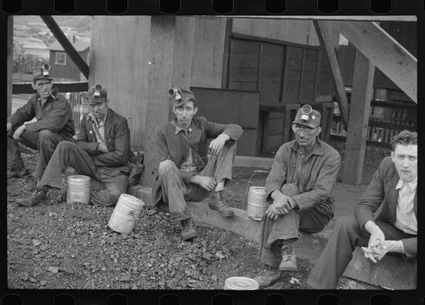 Black and white photo of five coal miners sitting on ground