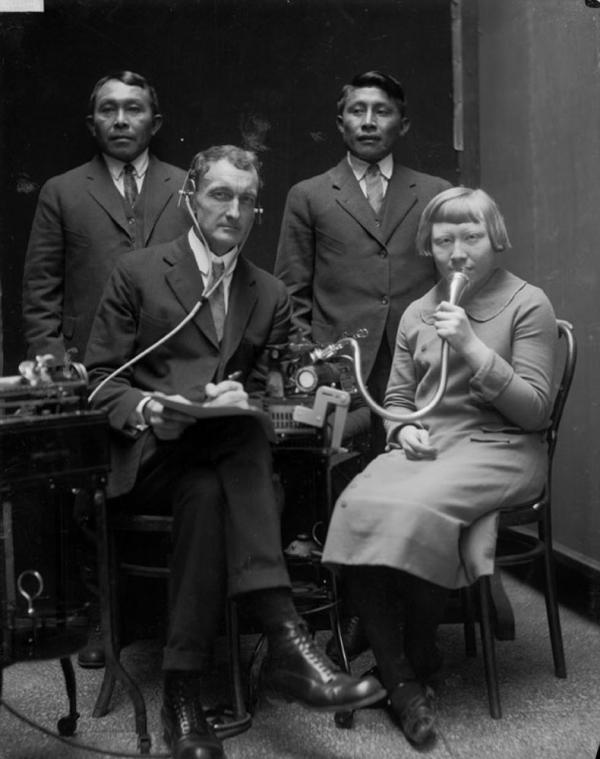 Black and white photo of men and a woman speaking into microphone