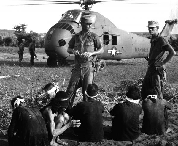 Viet Cong prisoners wait in front of a U.S. Marine Corps Sikorsky UH-34D Seahorse helicopter.