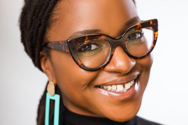 Headshot of a smiling Black woman wearing glasses in a black turtleneck in front of a white background