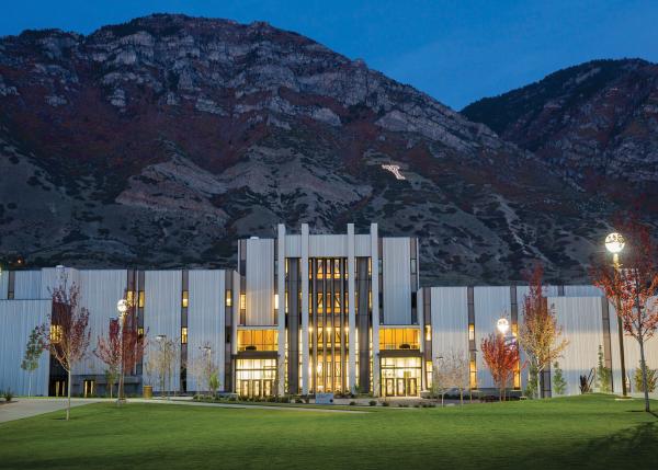 A photograph of the illuminated BYU law school at dusk with mountains in the background.