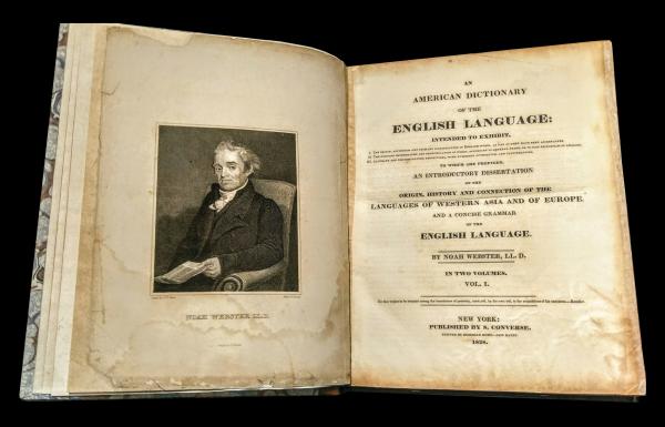 Photo of American Dictionary of the English language opened to the title page, with an illustration of Noah Webster on the left.
