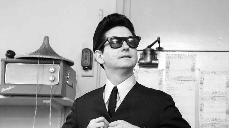 Black and white photo of a man in sunglasses buttoning a jacket