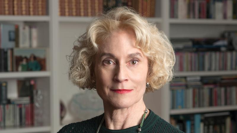 A portrait photo of Martha Nussbaum standing in front of a large bookcase. 