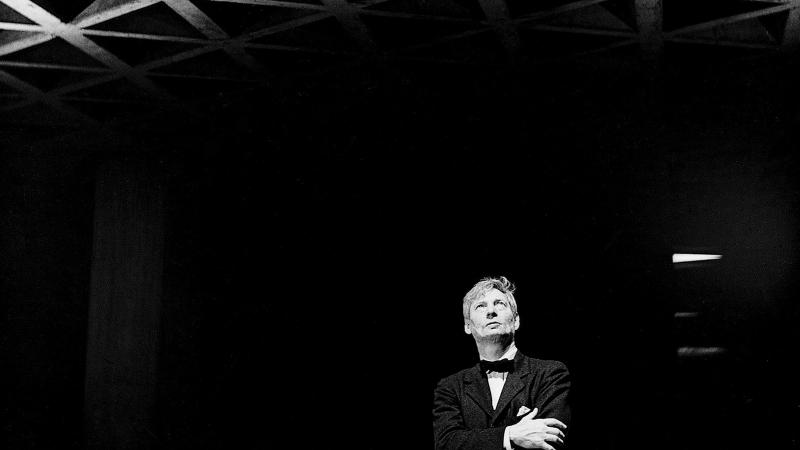 Black and white photo of Louis Kahn standing in a dark room, looking at a decorative ceiling. 