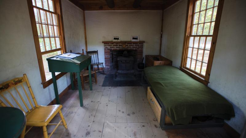 Picture of a basic bedroom with a fireplace, cot, and writing desk.