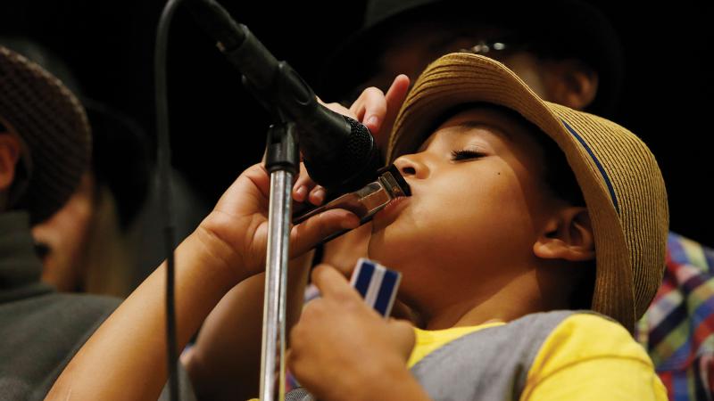 A student plays a harmonica into a microphone during the ABP's program