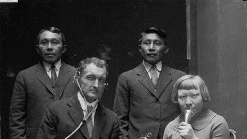 Black and white photo of men and a woman speaking into microphone