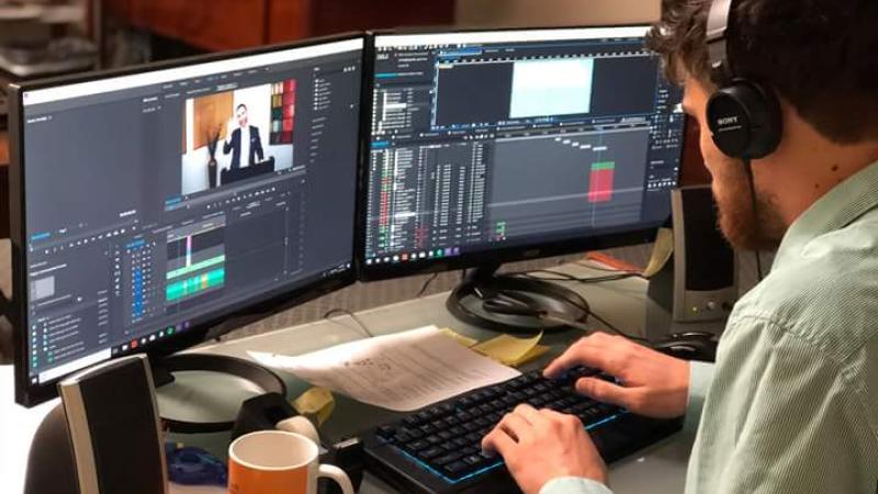 Man sitting at two computers, working on editing video