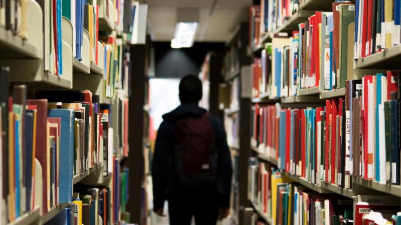 Bookshelves in foreground, man facing away at end of aisle