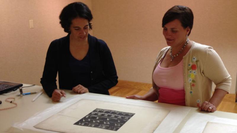 two women look down at piece of art on table