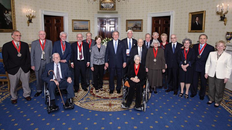President Bush, standing in the middle of the Medalists wearing their medals, in the Oval Office