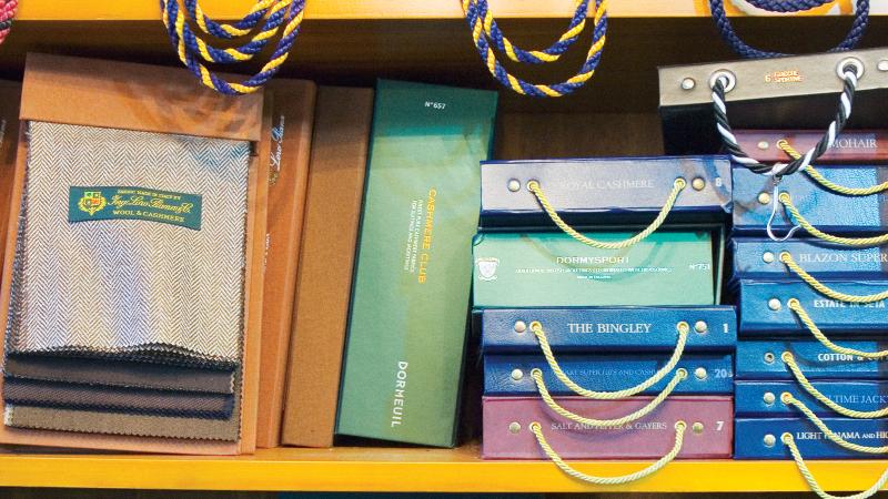 Three shelves stacked with books and logs dealing with fabric and suit tailoring styles