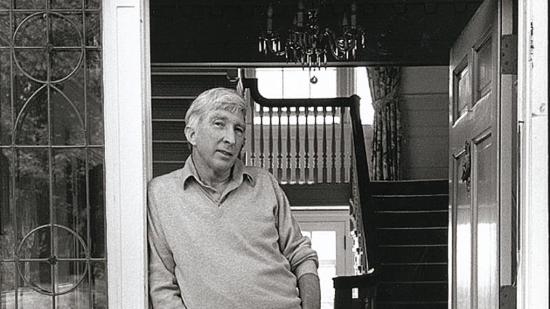 Black and white photo of man leaning against doorway