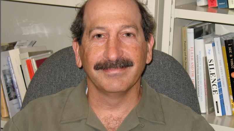 Photograph of man sitting in chair, bookshelves behind him